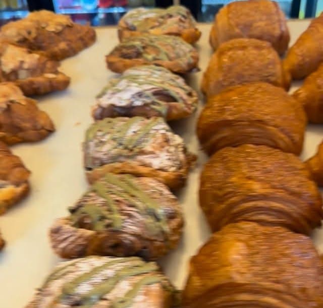 Rows of croissants and pistachio pastries lined up on the bakery counter