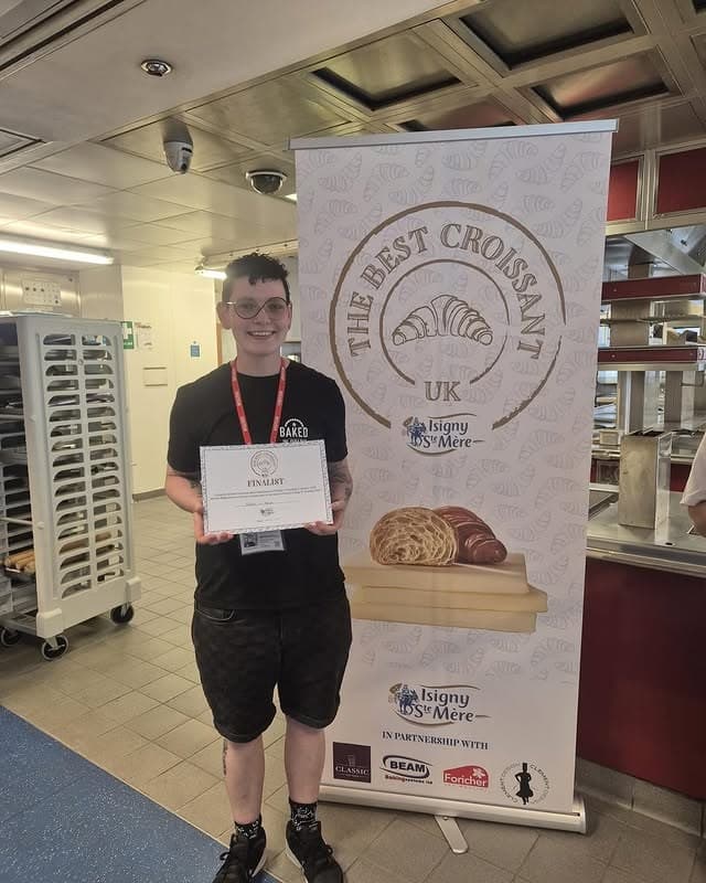 A Mason & Crumb baker holding the croissant award finalist certificate beside the award banner