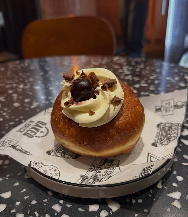 A cherry brioche doughnut topped with cream on bakehouse paper